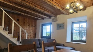 Ein rustikales Interieur mit einer Holztreppe, einem Esstisch mit Stühlen und zwei Fenstern mit Aussicht.