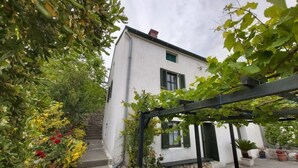Ein weißes Gebäude mit grünen Fensterläden, einer Steintreppe und einer mit Wein bewachsenen Pergola.