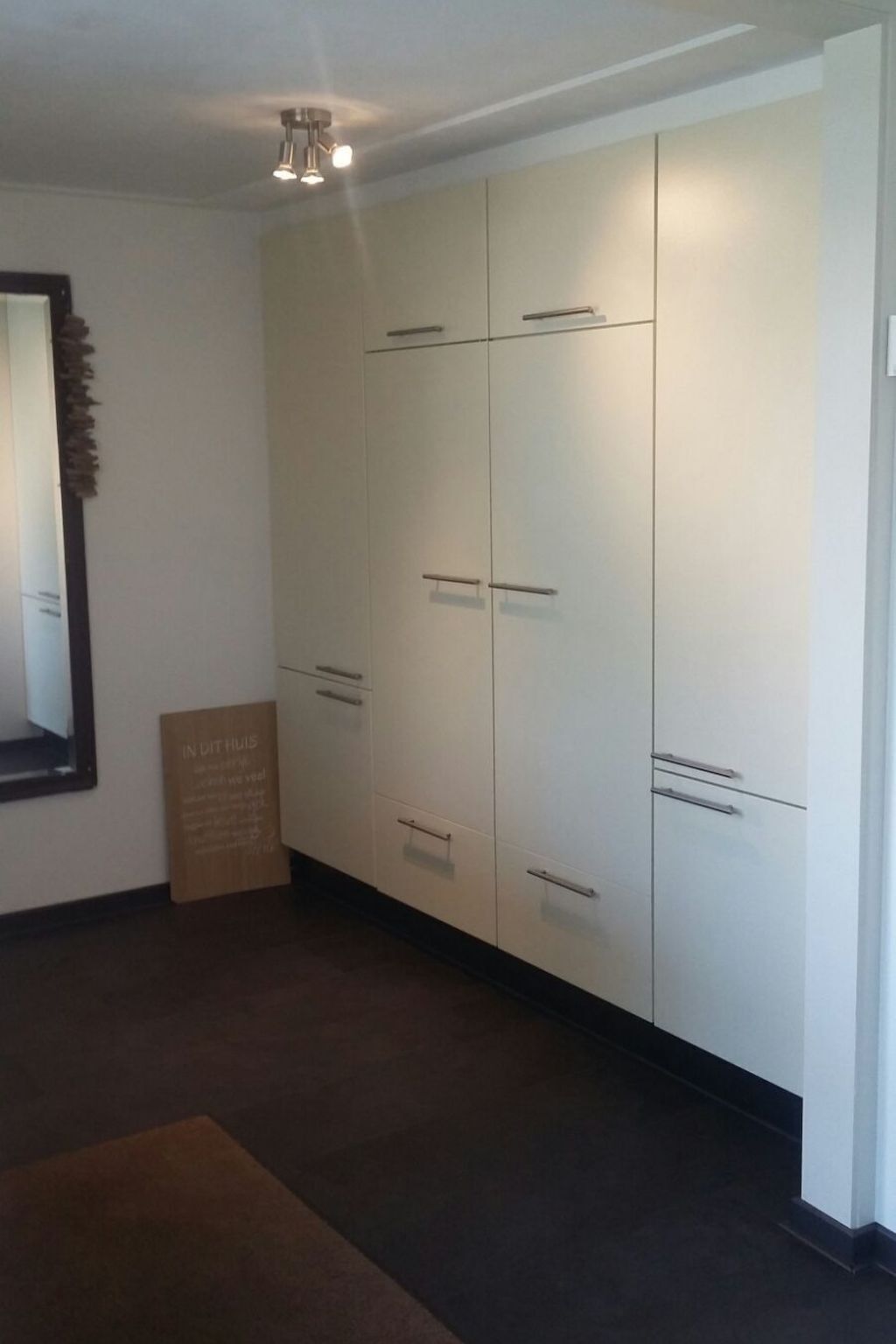 Een kamer met een grote witte garderobe, een spiegel en een bruin vloerkleed.