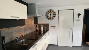 Una cucina moderna con un piano di lavoro nero, pensili bianchi, un lavandino in acciaio inossidabile e una cappa aspirante integrata. Si nota una sveglia a parete e una porta con un piccolo decoro a testa di toro.