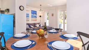 Een eethoek met een ronde houten tafel gedekt voor vier personen, omgeven door blauwe placemats en witte borden. Er staan wijnglazen en een fruitmand op de tafel.