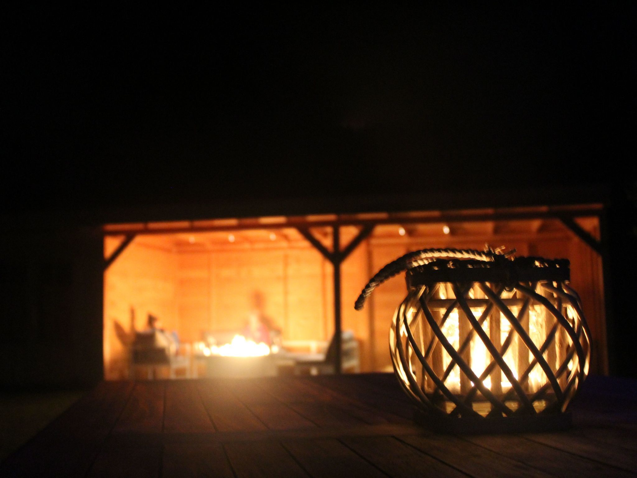 Ein Laternenlicht auf einem Holzboden, im Hintergrund schimmert ein warmes Feuer.