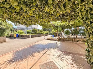 Un espace extérieur aménagé avec un revêtement pavé et un sol carrelé, entouré de verdure et d’arbres.