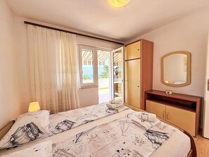 A bedroom with a bed, a bedside table, a mirror, and a view of the outdoors. - Apartment Dragica by Interhome (Polje)
