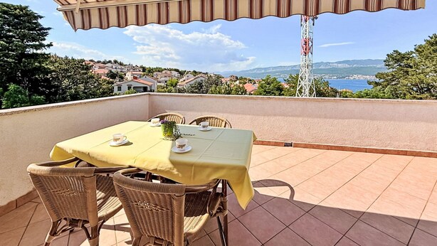 A terrace with a table and chairs, a striped awning, and a view of a coastal town. - Apartment Dragica by Interhome (Polje)