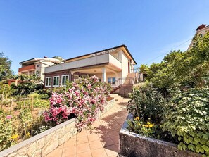 A two-story house with a balcony, a stone pathway, and lush greenery. - Apartment Dragica by Interhome (Polje)