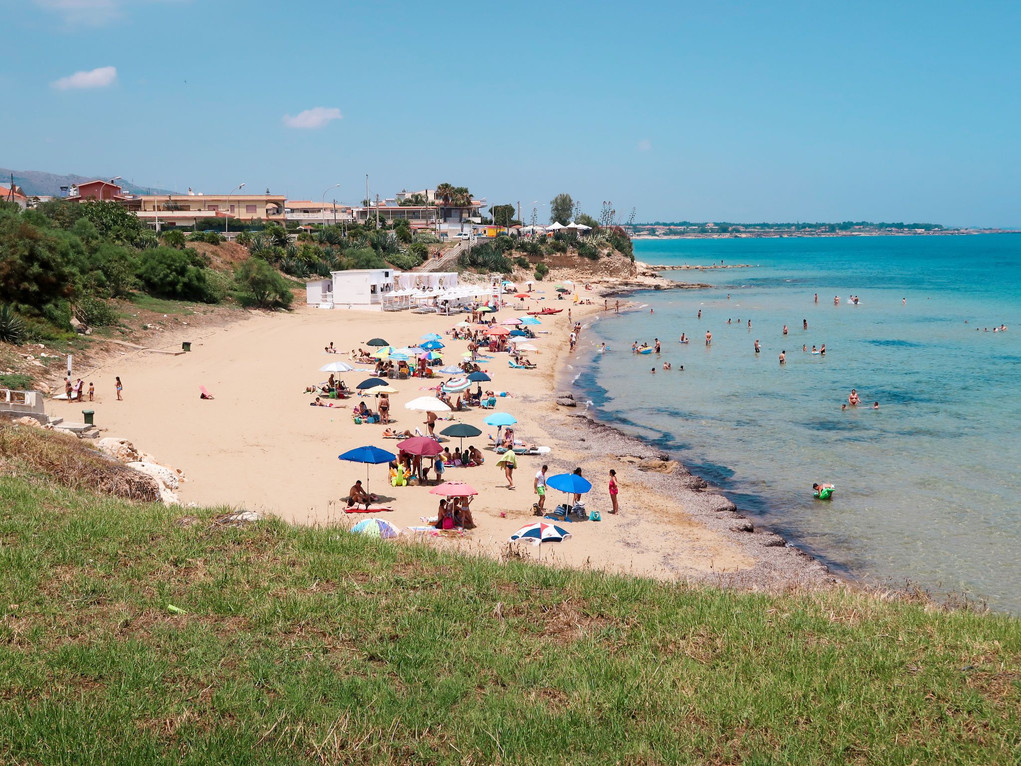 A beach with people sunbathing and swimming, umbrellas, and a clear view of the sea.