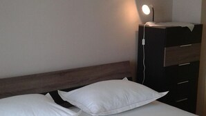 Ein Bett mit weißer Bettwäsche und zwei Kissen, ein Nachttisch mit einer Lampe und ein Holz-Kopfstück.