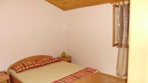 Ein Schlafzimmer mit einem hölzernen Bett, einem Nachttisch, einer Lampe und einem Fenster mit Vorhang.