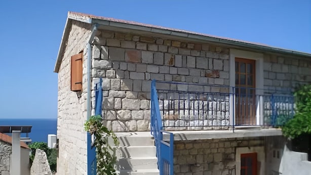 Ein Steinhaus mit Balkon, einer roten Tür und Blick auf das Meer.