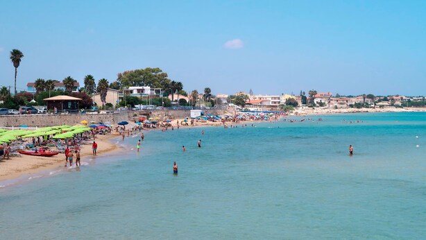 Ein Strand mit klarem, blauem Wasser, Sonnenschirmen und badenden Personen.