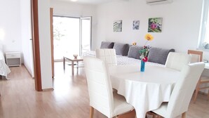 A dining area with a round table and white chairs, a sofa with grey cushions, and a vase with flowers on the table. - Helle Wohnung in Selce mit Terrasse by Interhome (Selce)