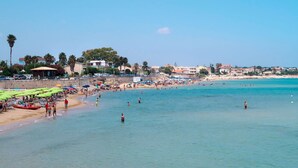 A beach with clear blue water, umbrellas, and people swimming. - Wohnung 'Cicirata Sea Beach by Interhome (Avola)