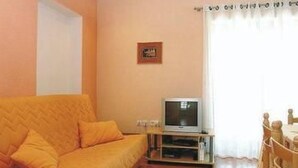 Una sala de estar con sofá, televisión sobre un mueble bajo y una mesa de comedor con sillas.