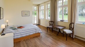Een slaapkamer met een bed, twee stoelen, een tafel en grote ramen.