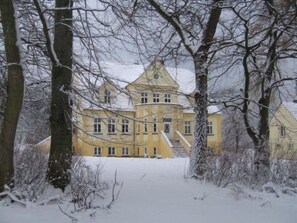 A large, yellow building with multiple windows and a central staircase, surrounded by snow-covered trees. - Wohnung in der ersten Etage des Herrenhauses by Interhome (Gingst)