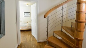 Eine Holztreppe mit Metallgeländern führt zu einem Schlafzimmer, das ein Bett und ein gerahmtes Bild zeigt.