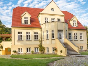 A large, yellow building with a red roof, multiple windows, and a staircase leading to the entrance. - Wohnung im Erdgeschoss des Gutshauses by Interhome (Gingst)