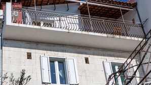Un edificio a due piani con un balcone, una finestra con persiane e un muro in mattoni ben visibile.