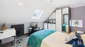 Een moderne slaapkamer met dakraam, bureau, bed met groene deken en grote spiegel.