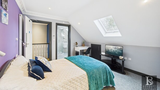 Een slaapkamer met een bed, een bureau, een stoel, een televisie, een dakraam en een badkamer met een glazen deur.
