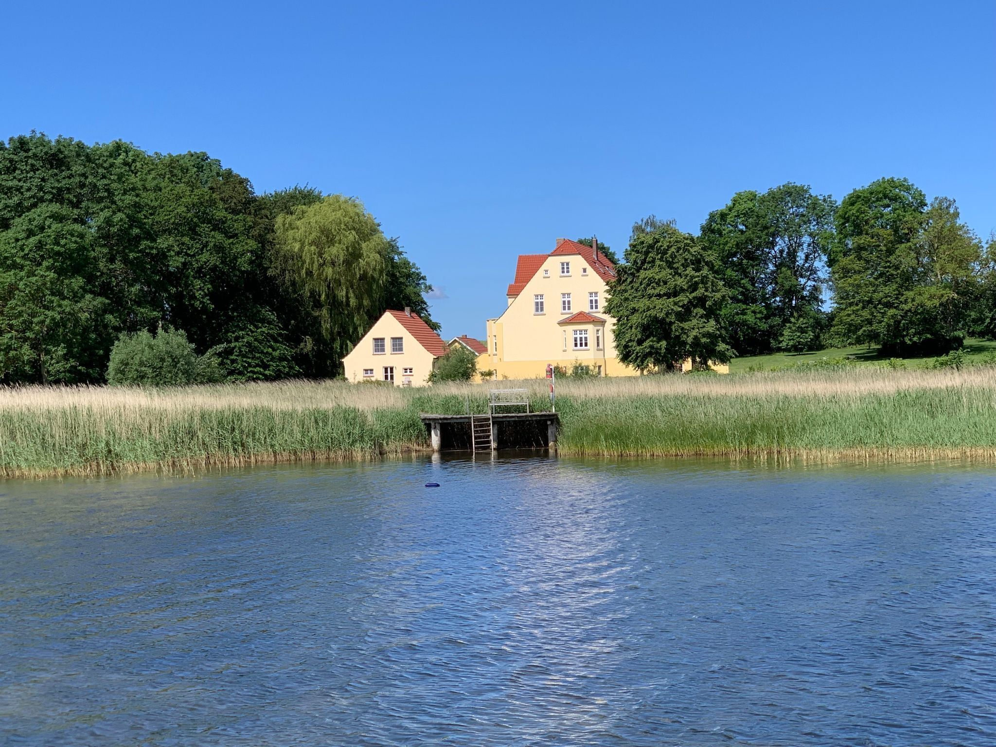 A house with a red roof and a dock extending into a calm body of water.