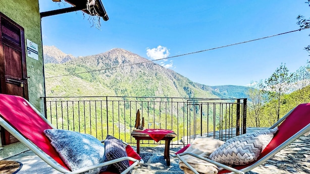 Ein Balkon mit zwei Liegestühlen, einem kleinen Tisch und Blick auf Berge.