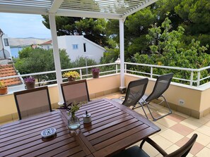 A covered outdoor seating area with a table and chairs, potted plants, and a view of the sea and hills. - für 3 Personen  + 1 Kind ca. 68 m² in Žaboric, Dalmatien (Gespanschaft Sib by Interhome (Brodarica/Žaborić)
