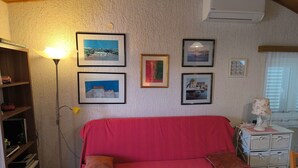 A cozy room with a red sofa, a floor lamp, and a bookshelf. There are framed pictures on the wall and an air conditioner above. - für 3 Personen  + 1 Kind ca. 68 m² in Žaboric, Dalmatien (Gespanschaft Sib by Interhome (Brodarica/Žaborić)