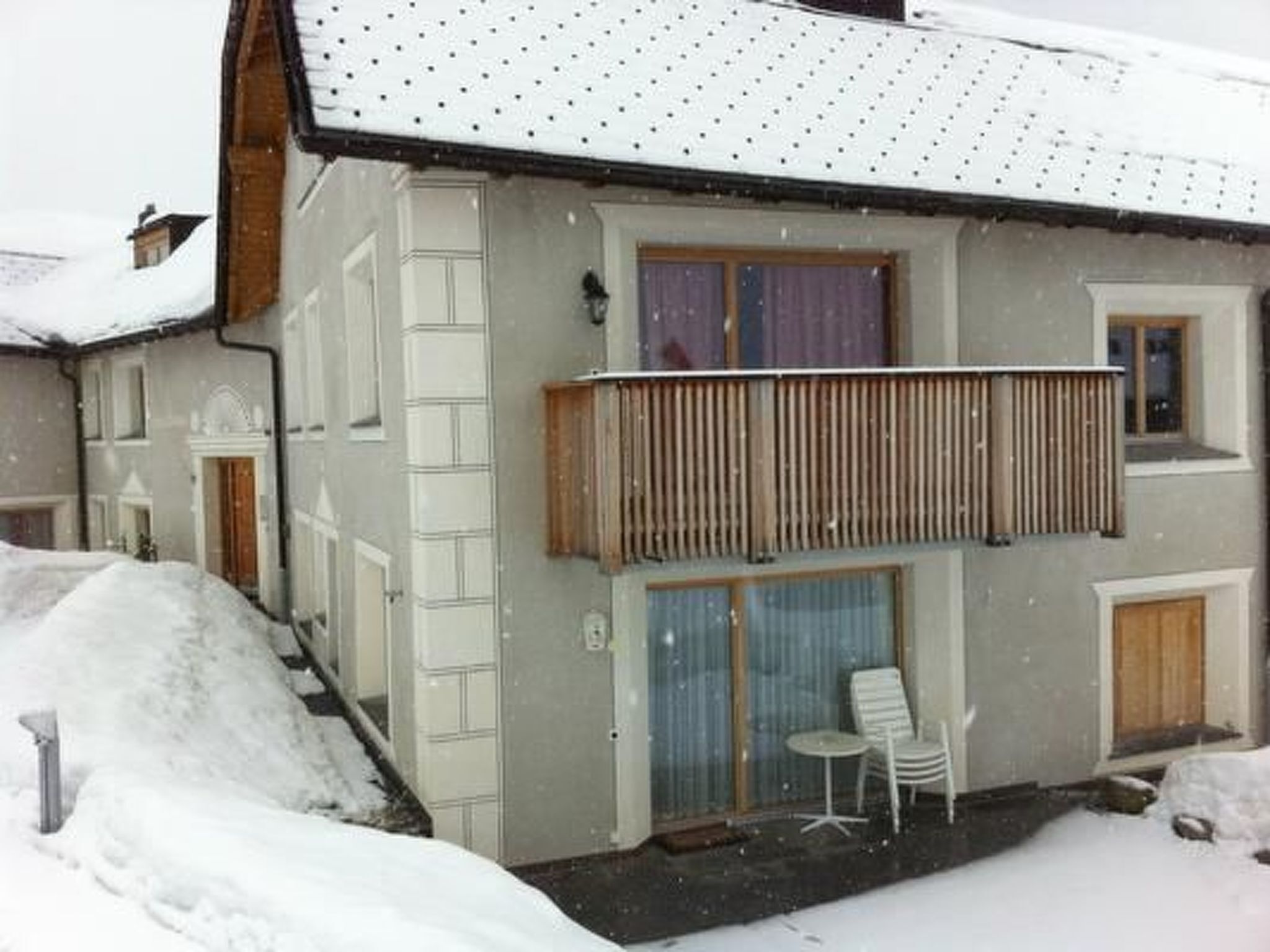 Ein zweistöckiges Gebäude mit einem Balkon, einer überdachten Sitzterrasse und einem mit Schnee bedeckten Dach.