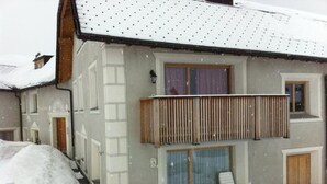 A two-story building with a balcony, a covered outdoor seating area, and a snow-covered roof. - Chesa Lodola by Interhome (Madulain)