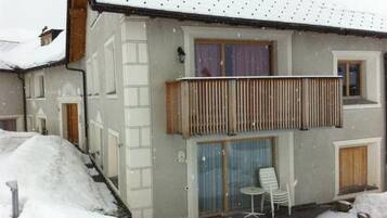 Ein zweistöckiges Gebäude mit einem Balkon, einer überdachten Sitzterrasse und einem mit Schnee bedeckten Dach.