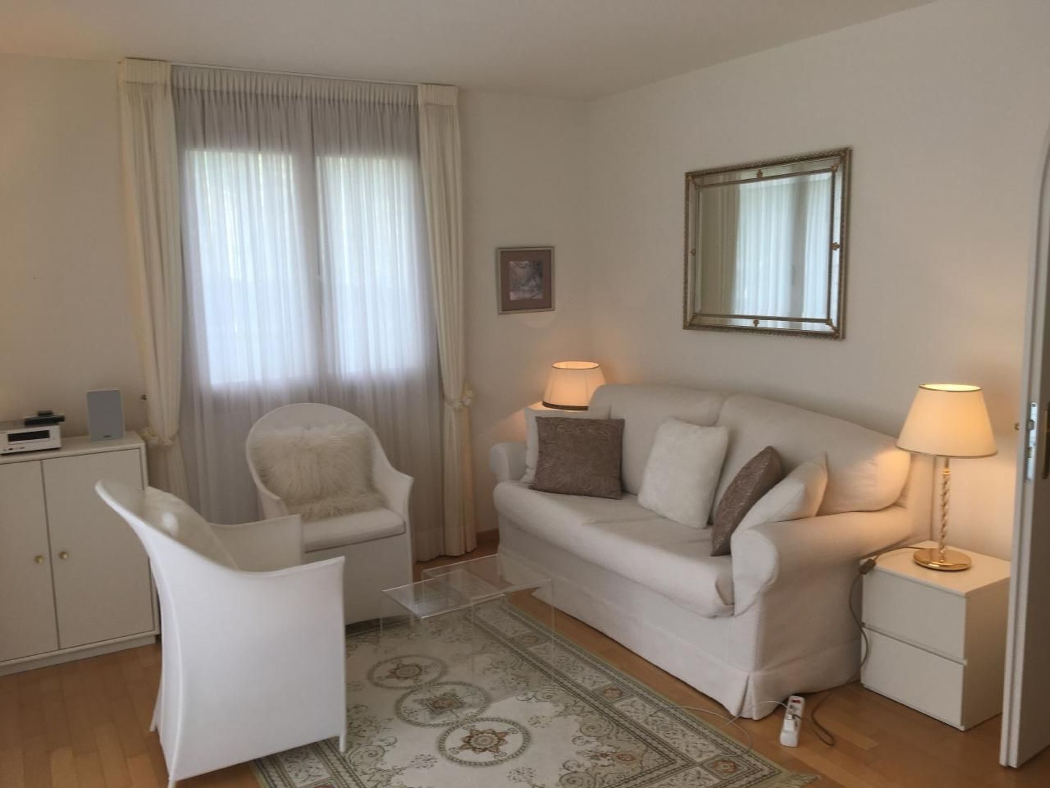 Ein Wohnzimmer mit einer Couch, zwei Sesseln, einem kleinen Tisch, einer Lampe, einem Spiegel und einem Schrank.