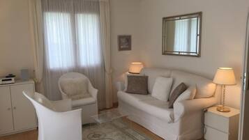Ein Wohnzimmer mit einer Couch, zwei Sesseln, einem kleinen Tisch, einer Lampe, einem Spiegel und einem Schrank.