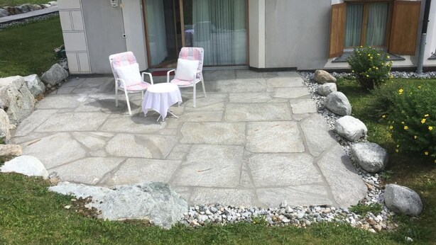 A patio with stone flooring, two white chairs, and a small round table. - Chesa Lodola by Interhome (Madulain)