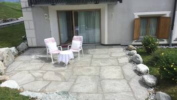 Eine Terrasse mit Steinboden, zwei weißen Stühlen und einem kleinen runden Tisch.