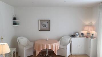 Ein gemütliches Zimmer mit einem runden Tisch, zwei Stühlen, einer Kommode und einem gerahmten Bild an der Wand.