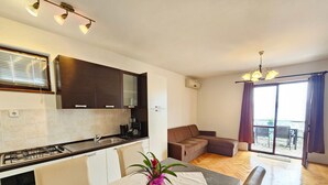 Eine moderne Küche mit Gaskochfeld, Spüle und dunklen Holzschränken. Es gibt eine Essecke mit Tisch und Stühlen, und ein Sofa im Wohnzimmer.