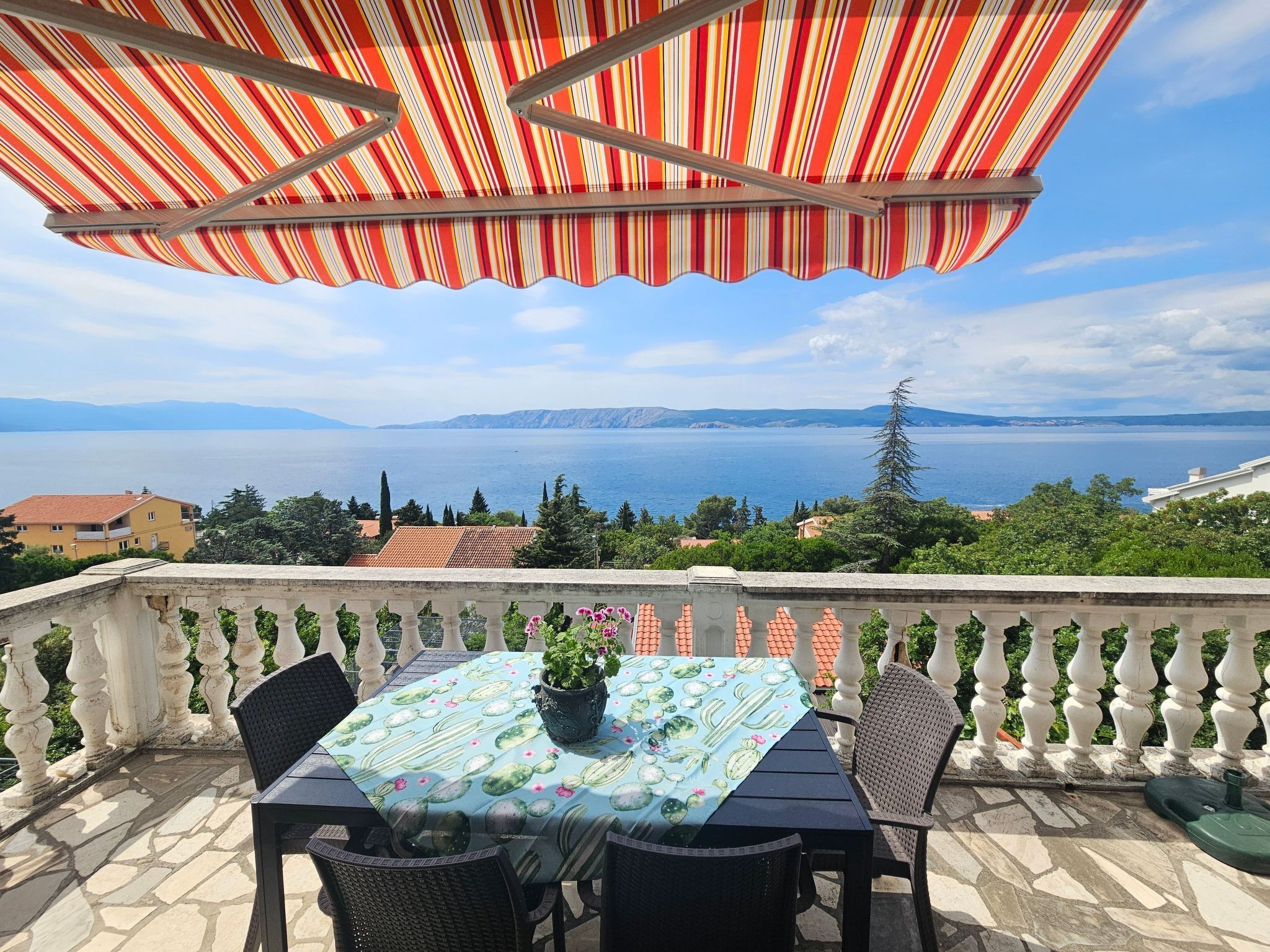Un balcon avec une table et des chaises, offrant une vue panoramique sur une étendue d’eau et des montagnes lointaines.