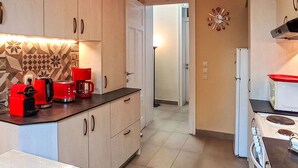 Een keuken met lichtkleurige kastjes, een rode koffiezetapparaat, een witte kookplaat en een decoratieve spatwand.