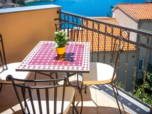 Ein Balkon mit Tisch und Stühlen, einem Blumentopf und Blick aufs Meer.