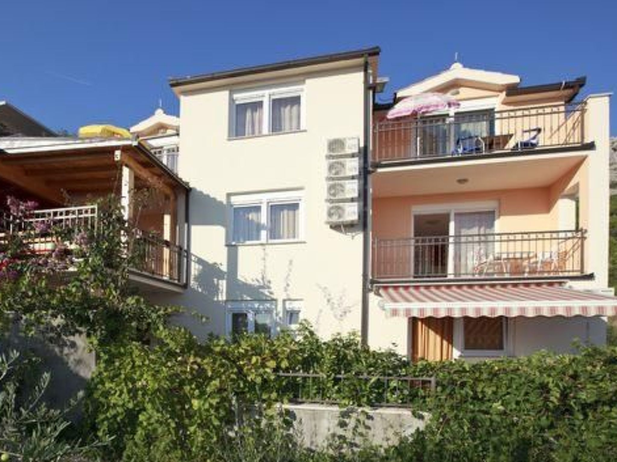 A multi-story residential building with balconies, a garden area, and a clear sky.