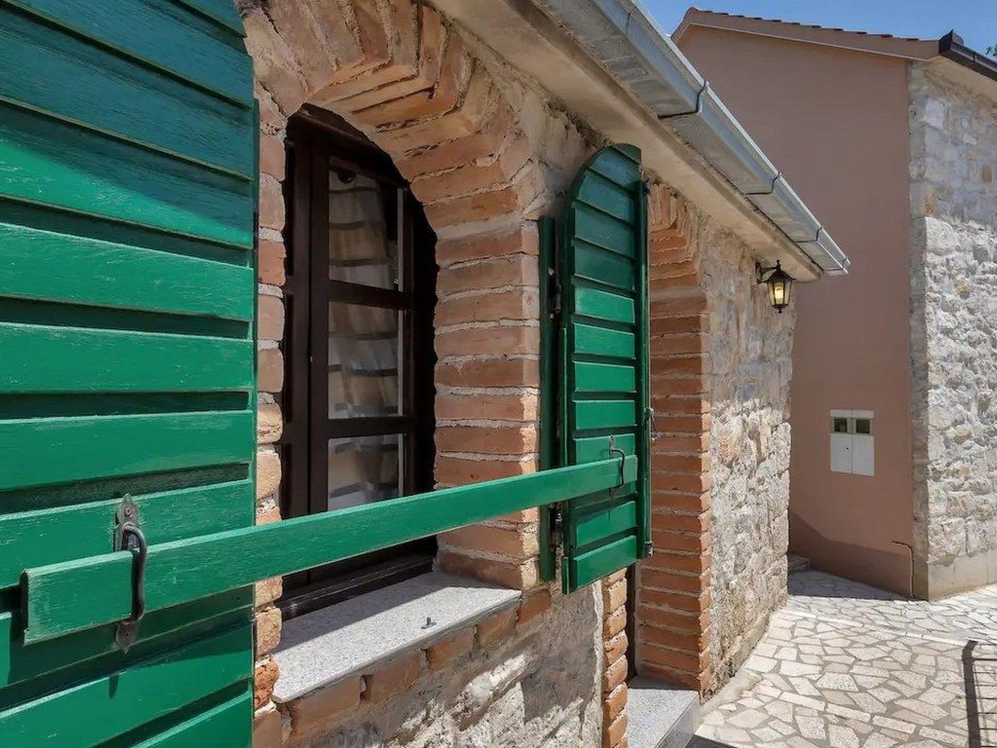 A traditional stone building with green shutters, a small window, and a tiled entrance.