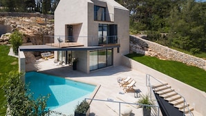 Une maison moderne à deux étages, dotée d’une piscine, d’un espace salon extérieur et d’un escalier menant à un balcon.