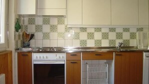 A kitchen with white cabinets, a stove, and a tiled backsplash. - Suot Rövens by Interhome (Samedan)