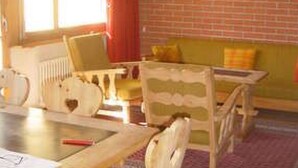 A cozy room with a brick wall, a wooden ceiling, and a window with curtains. There is a table with chairs and a sofa. - Suot Rövens by Interhome (Samedan)