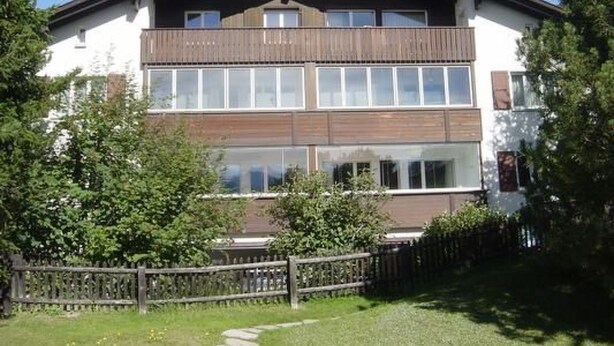 A two-story building with a wooden balcony, large windows, and a fenced yard. - Suot Rövens by Interhome (Samedan)