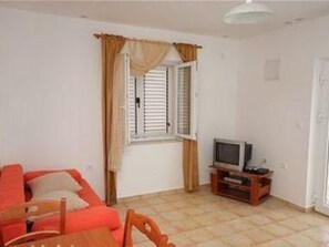 A room with a red sofa, a television on a wooden stand, and a window with curtains. - Kleines Apartment Emil Vanily by Interhome (Dragišina)