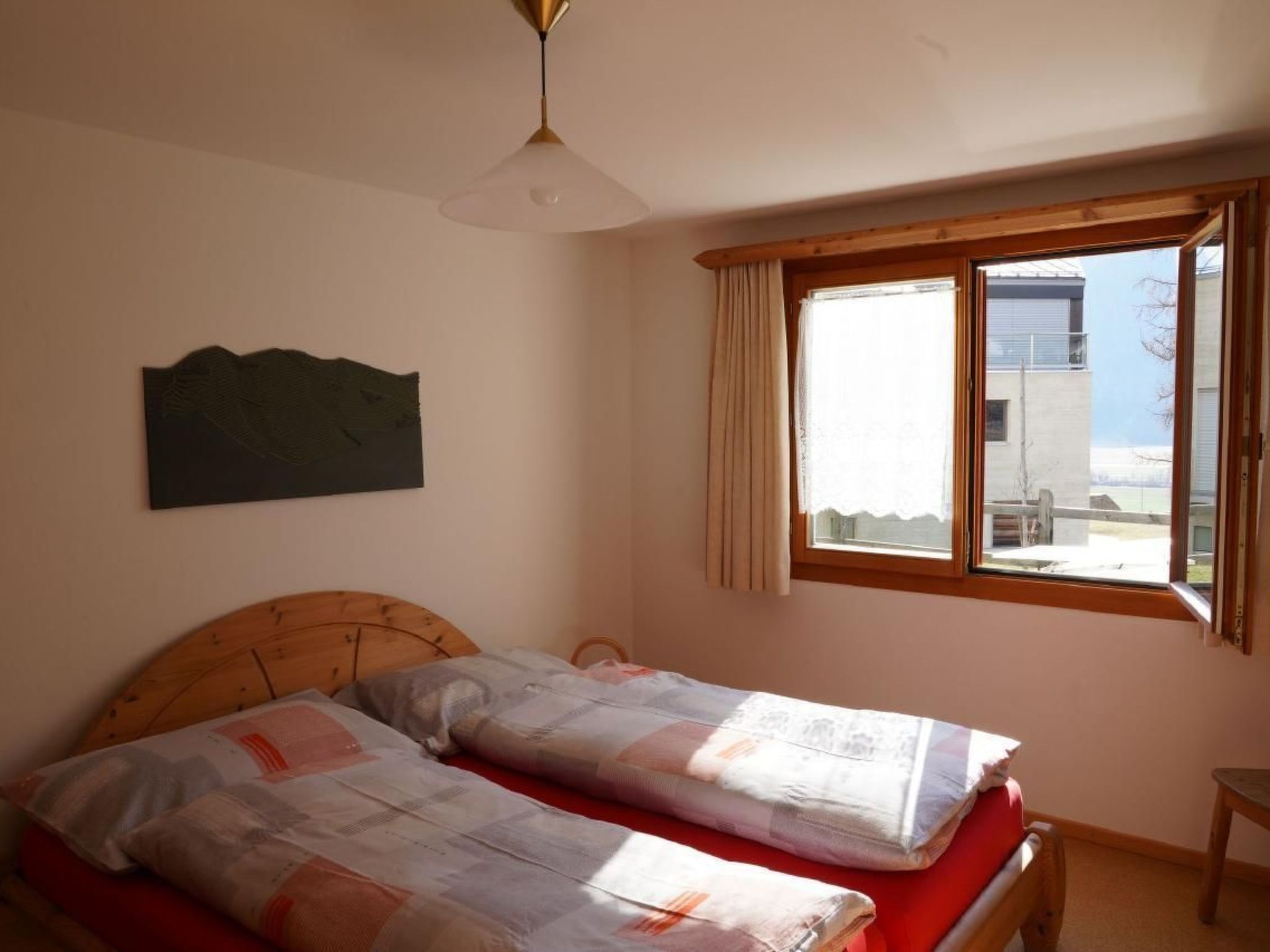 A bedroom with two beds, a wooden headboard, a ceiling fan, a window with curtains, and a view of the outside.