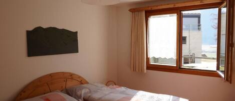A bedroom with two beds, a wooden headboard, a ceiling fan, a window with curtains, and a view of the outside.